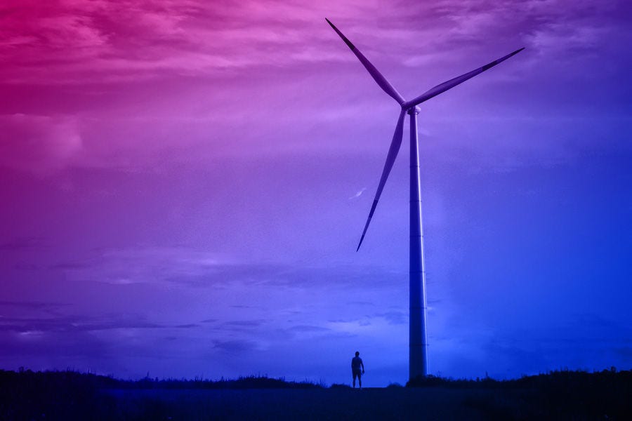 A wind turbine against a dark sky, a small silhouette of a man next to it